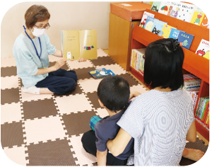 女性がこどもを膝に乗せて座り、語り部の読み聞かせに聴き入っている写真