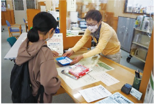 カウンターで本を手渡す図書館職員とそれを受け取るリュックサックを担いだ女の子の写真