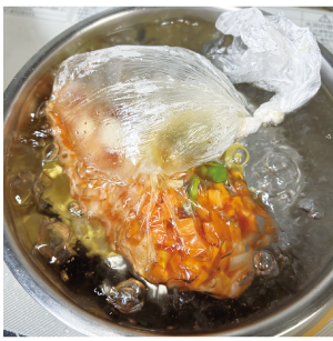 具材の入ったポリ袋を皿を敷いた鍋に入れて加熱している写真