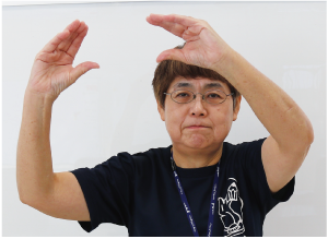 手話通訳者鈴木さんが頭の上で手の平を広げてからすぼめている写真