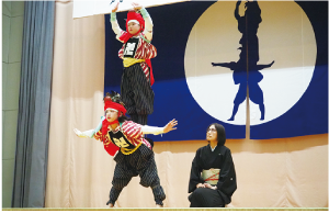 土台の人は四つん這い、その上に両手を頭上にあげた人が立ち、２人で組になって角兵衛獅子の技を披露している写真