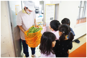 収穫した野菜を調理室へ届けている写真