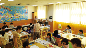 大人が宿題をしているこどもたちを見守っている写真