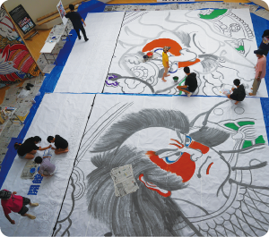 大凧に描かれた武者絵の色塗りをしている様子を上から撮影した写真