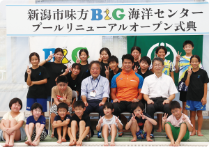 オレンジと青のアルビレックスカラーのTシャツを着た水沼尚輝選手と水泳教室に参加したこどもたちの集合写真