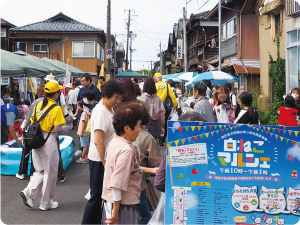 いくつか並ぶ簡易テントの店舗前を往来するたくさんの買い物客で賑わう小路の写真