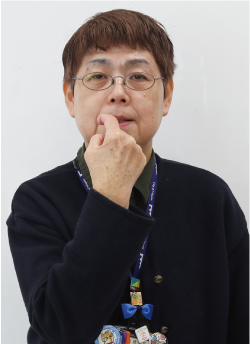 手話通訳者鈴木さんが歯を見せながら人さし指を右から左に動かしている写真