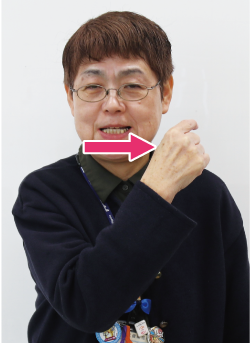 手話通訳者鈴木さんが歯を見せながら人さし指を右から左に動かしている写真