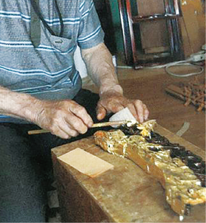 彫刻が施された材料にピンセットを使い、金箔を貼っている写真