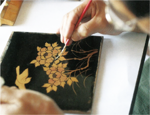 漆塗りが終わった材料に細い筆を使い絵を描いている写真