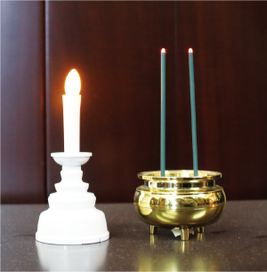 炎が電池式のろうそくが立てられた白い燭台と先端の火が付いた部分が電池式の線香が立てられた線香立ての写真