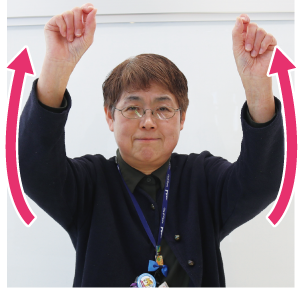 手話通訳者鈴木さんが両手の親指と人差し指をくっ付けて頭の上にあげている写真