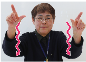 手話通訳者鈴木さんが人さし指を離して広げ、その手をジグザクにしながら頭の上から下へ移動させている写真