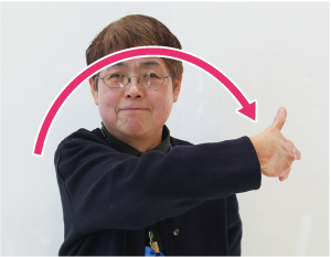手話通訳者鈴木さんが「数字の７」を表現しながら、その手を右から左に半円を描きながら移動させている写真