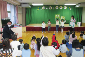 白根保育園園児４人が前に並び、そのうち２人がホウレンソウとハクサイの絵が付いたボードを頭の上に掲げ、ブロッコリークイズをしている写真