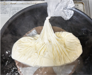 お湯の入った鍋底に皿を敷き、その上に材料の入ったポリ袋を乗せている写真