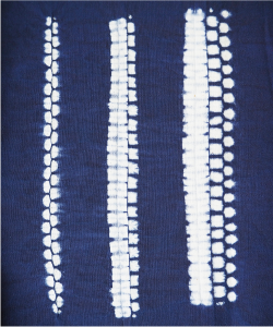 折り縫い絞りの写真 布を折りたたみ絞り糸を縫うことで、規則的な模様を作ります。小さな白い四角や丸、楕円の模様が縦に並んでいます。