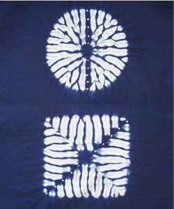 合わせ縫い絞りの写真 布を合わせ縫う絞りです。丸と四角の白い模様があり、中心から外側に向かって放射状に藍色の線が入っています。