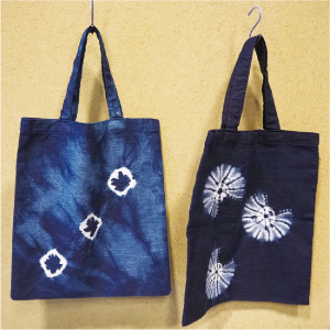トートバッグの写真 二つトートバッグがあり、１つ目は薄い藍色に、斜めに3つ白い四角が並んだ模様です。2つ目は濃い藍色で、白く放射線状の模様が入った丸が3つあります。