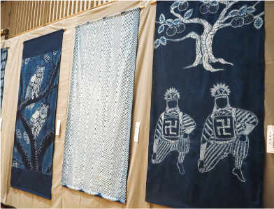 タペストリーが3枚並んだ写真 右側が月潟の角兵衛獅子の模様、中央が白地に藍色のジグザグした線が一面に並べられた模様、左側が二匹のフクロウが木にとまっている模様です