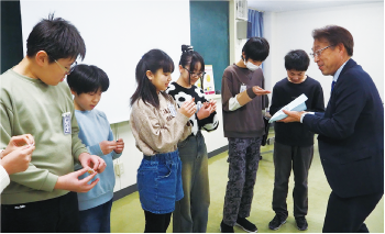 横並びに並んだ新飯田小学校６年生に長浜区長が缶バッチを渡している写真