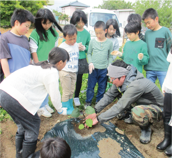 農家さんに指導を受けながら、野菜の植え方を学ぶ大鷲小学校の児童の写真