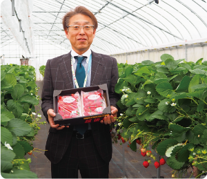 区長が越後姫のパックを持って、越後姫のハウスの中で笑っている写真