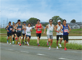 水を張った田んぼの脇を列になって走り抜けるランナーたちの写真