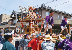 神輿を担ぐ人たちと神輿の持ち手に立つ二人の男の子の写真