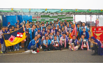 青い法被を着た多くの人と優勝旗や優勝カップを持つ人たちの集合写真