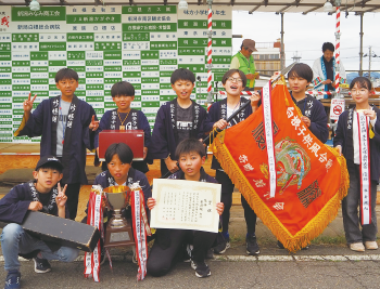 賞状、優勝カップ、優勝旗を持っている黒い法被を着たこどもたちの集合写真