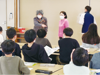 教室で児童が前を向き、講師の話を聞いている写真