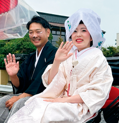 白無垢を着た女性と狸のメイクをした袴を着た男性が手を振っている写真