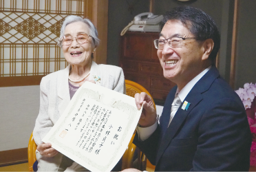 椅子に座って症状を持つ高齢の女性と中原市長の写真