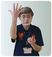 手話通訳者・鈴木さんが片手をパーにして頭の高さへ、もう片方の手は胸の前でグーにしている写真