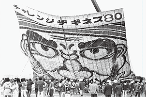 161畳のチャレンジギネス80凧の前にたくさんの揚げ手が並び、凧の圧倒的な大きさが分かる写真